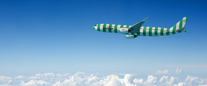 Grün-weiß gestreiftes Condor-Flugzeug am Himmel, umgeben von hellblauem Himmel mit Wolken unterhalb der Maschine.